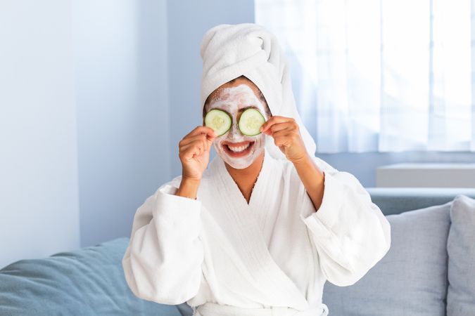 Woman in bathrobe holding cucumbers to her eyes
