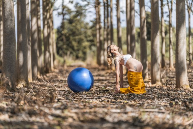 Adult pregnant woman training with pilates ball in park during sunny day