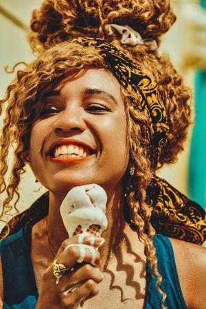Close up of smiling Black female smiling with an ice cream cone in the sun, vertical