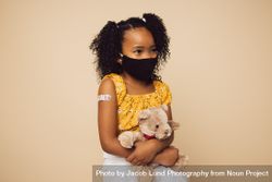 Small girl wearing protective face mask sitting with her teddy bear bEKNn5