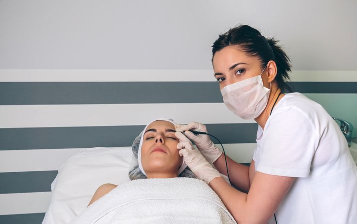 Woman receiving treatment on face in clinical center from aesthetician