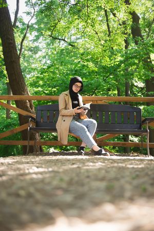 Woman in headscarf relaxing in park with book