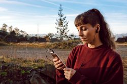 Young woman with piercing listening music on smartphone on hill