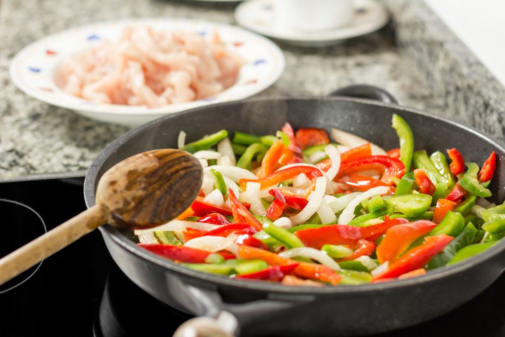 Closeup of female cooking vegetables and chicken in a pan