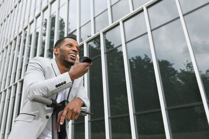 Smiling Black man riding scooter and speaking on smartphone