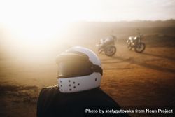 Biker helmet on dusty path with two bikes in background bD8d8b