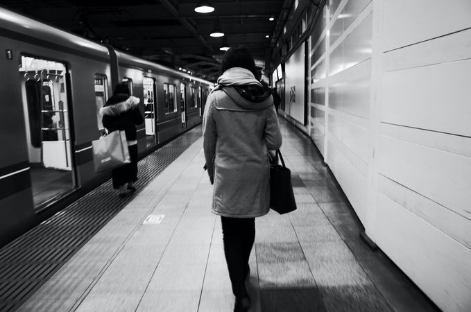 Grayscale photo of back view of woman walking in subway