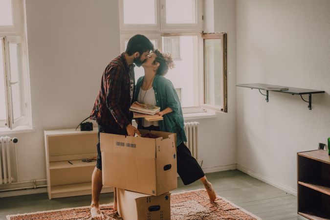 Casual couple unpacking boxes in apartment and kissing