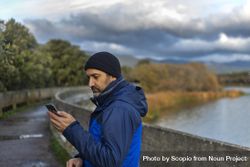 Man holding a phone standing beside waterside 5k8P64