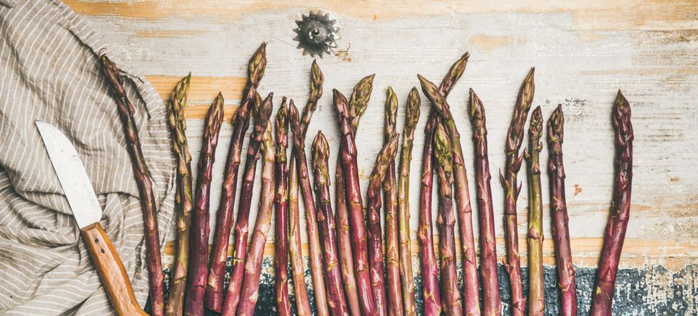 Lined up pieces of washed purple asparagus tips, on wooden board with linen