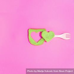 Green toast with heart cut out on a pink background with fork 4BoEBb