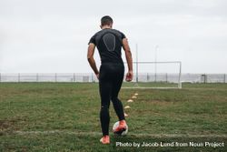 Rear view of a soccer player practicing dribbling with the help of cones arranged on field 5lOv60