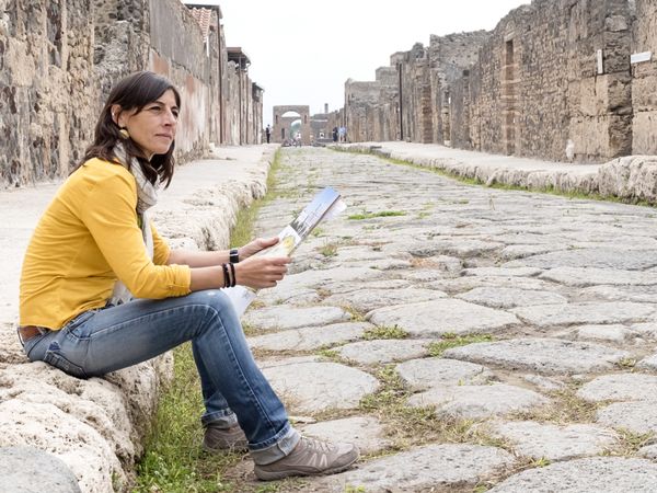 Side view of a woman in yellow clothes sitting while checking tourist map of ancient ruins