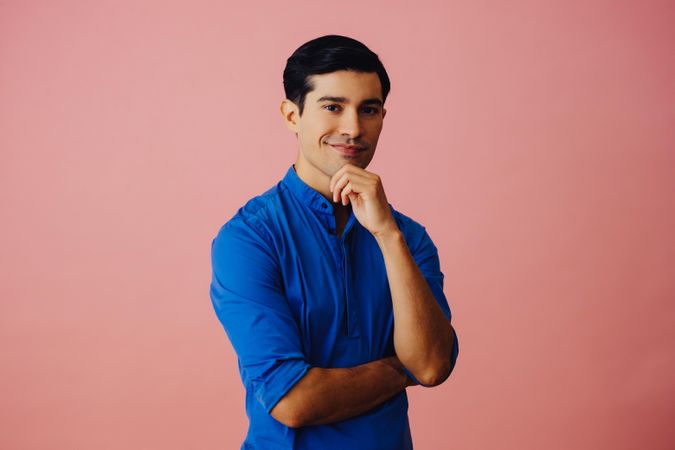 Medium shot of contemplative Latino man in pink studio with hand on chin