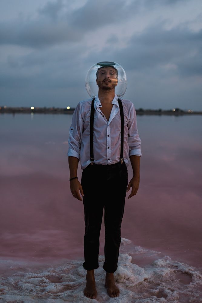 Man with fish tank on head standing at seashore