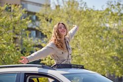 Smiling woman standing in car sunroof with outstretched arms