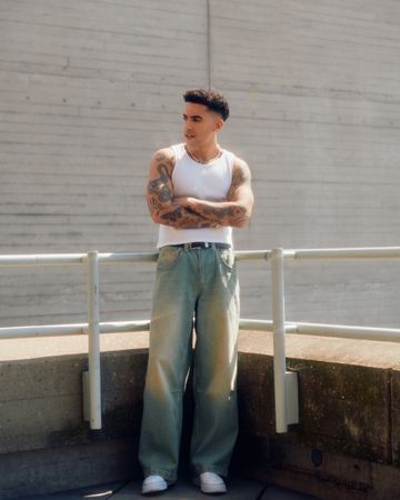 Man in vest and jeans standing with arms crossed among concrete structures