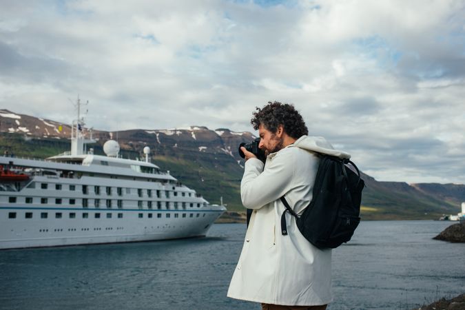 Man with backpack takes photo of cruise ship in port
