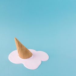 Melted pink ice cream and waffle cone on pastel blue background