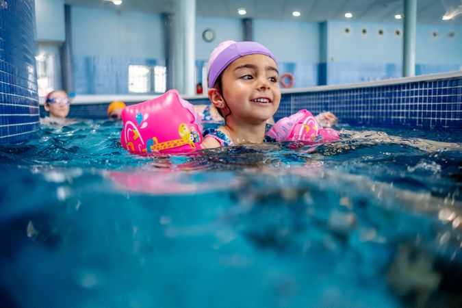 Cheerful girl in hat smiling and swimming in pool in water park
