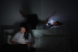 Woman and boy surfing gadgets in bedroom together