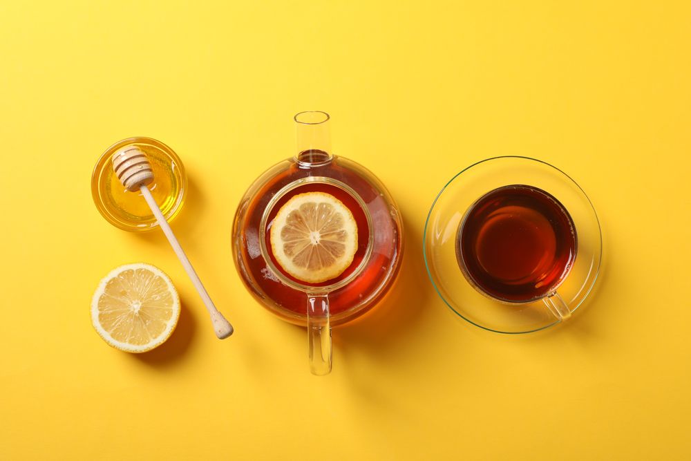 Flat lay. Cup of tea, teapot, lemon, honey and dipper on yellow background, copy space