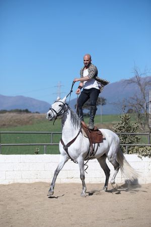 Man in checkered shirt standing up on saddle while riding horse