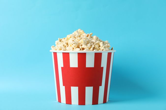 Striped bucket with popcorn on blue background, space for text