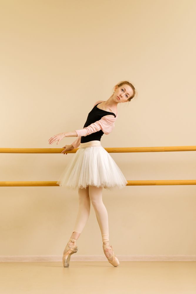 Ballet dancer performs on pointe, with hand on barre