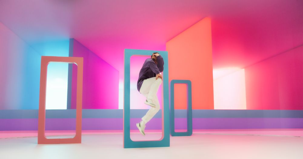 Young And Athletic White B-Boy Breakdancing To Break Beats in a Colorful Abstract Neon Lit Studio. Energetic Fashionable Male Dancer Talentedly Performing His Choreography On Multicolored Set.
