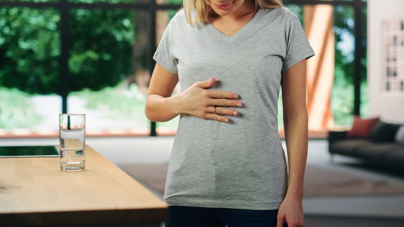 Young Adult Woman with Blond Hair Wearing Gray V-Neck T-Shirt, Rubbing Her Stomach After Food.