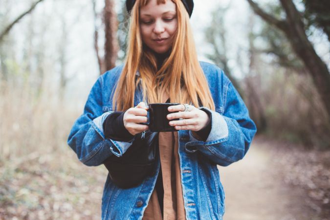 Woman looking down at her mug of coffee in the forest