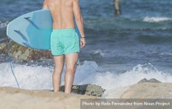 Legs and torso of male surfer with blue board approaching the water 0v6lx0