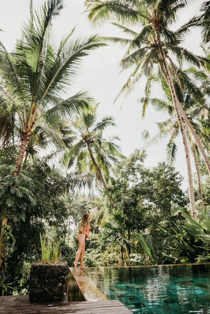 Blonde woman in bikini standing beside swimming pool surrounded by palm trees