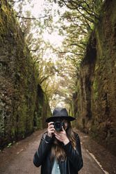 Young stylish woman taking photo on camera on way between high walls and trees