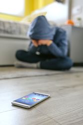 Teenager boy crying desperate for bullying with cell phone lying on the floor in foreground
