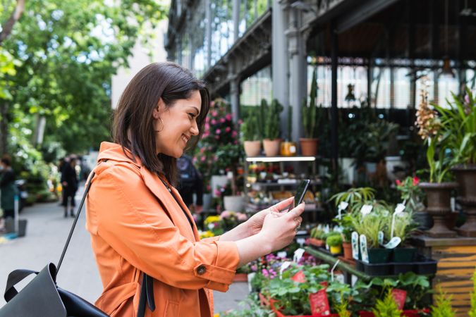Content woman taking photo of flowers in garden center