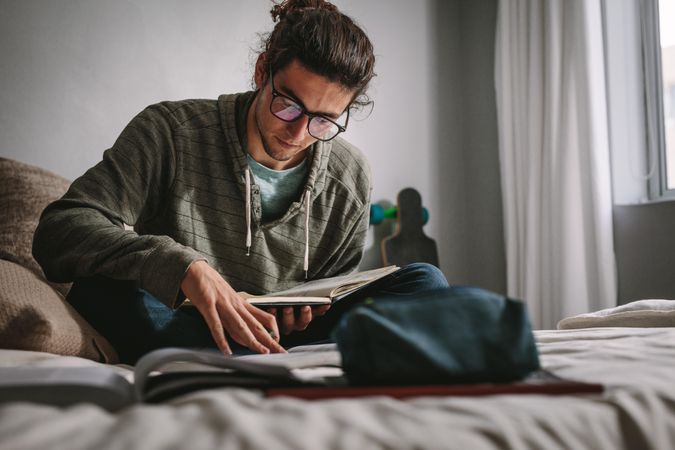 Student sitting on a bed and studying with focus and concentration
