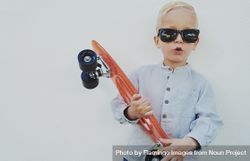 Young trendy blond boy leaning against a wall with red skateboard, copy space 0W3y10