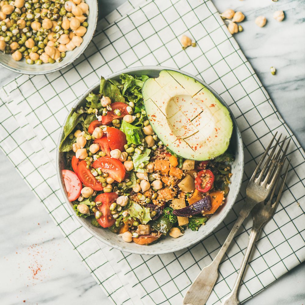 Healthy vegan lunch bowl with avocado, grains, vegetables, on checkered napkin, square crop