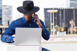 Serious businessman freelancer working on laptop and talking on mobile phone in city