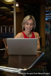 Smiling young woman in red tank top working on laptop computer in a coffee shop 43Elr0