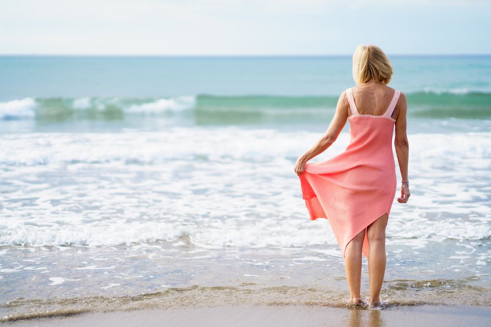 Back of mature woman standing on the beach facing the ocean, copy space