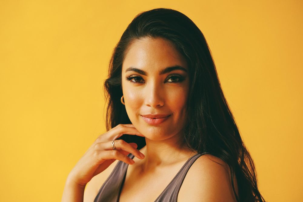 Hispanic woman looking at camera in yellow room with her hand to her chin