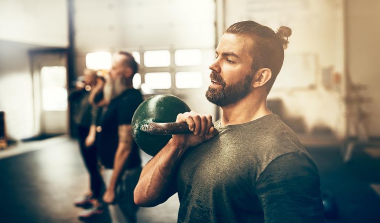 Man working out with group of people in class lifting kettlebells