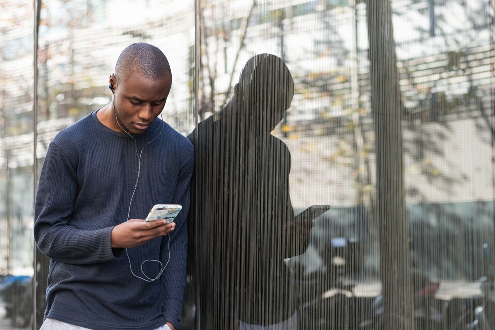 Serious Black man using smartphone against gray wall