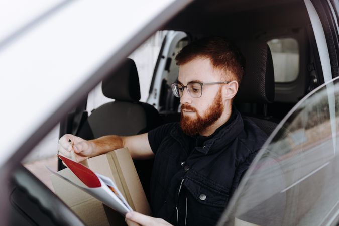 Courier filling papers while preparing for delivery of order to client in car