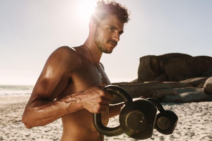 Man doing fitness workout at a beach using kettlebells