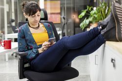 Smiling businesswoman with mug using smartphone