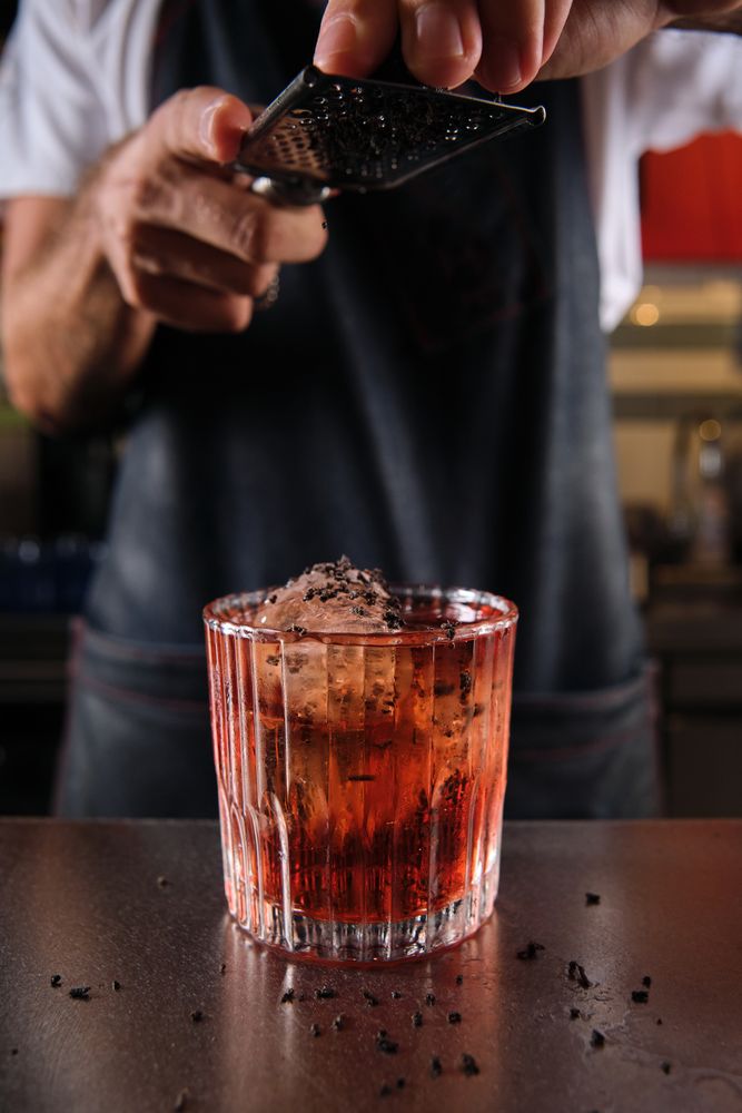 Unrecognizable bartender grating chocolate on Negroni cocktail